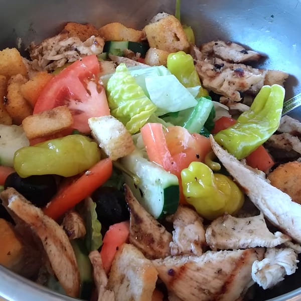 Close-up of an Italian salad with grilled chicken, tomatoes, cucumbers, lettuce, croutons, and peppers.
