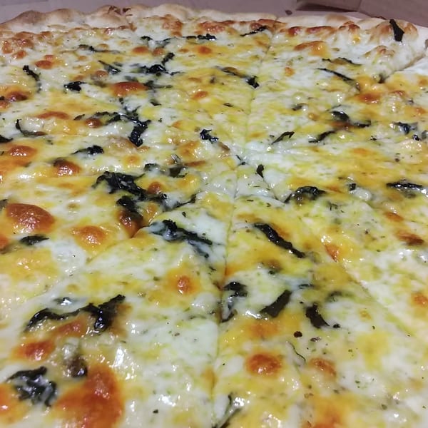 A close-up of a freshly baked Angelina's Trattoria pizza, topped with melted cheese and dark green herbs.