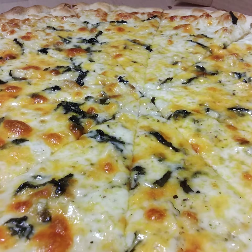 A close-up of a freshly baked Angelina's Trattoria pizza, topped with melted cheese and dark green herbs.