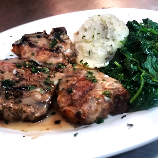 Pork chops with gravy, mashed potatoes, and sautéed spinach on a white plate at Angelina's Trattoria.