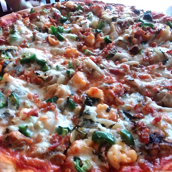 Close-up of a large Angelina's Trattoria pizza with shrimp, bacon, green peppers, and cheese.
